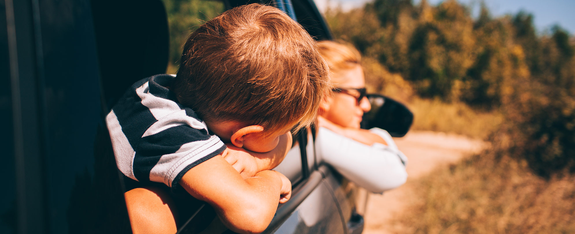 A mother and son are relaxing, while looking out of the windows of a car.