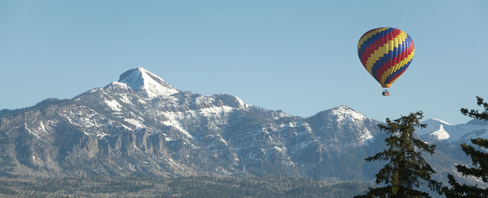 A colorful hot balloon flies high above the snowy mountains.