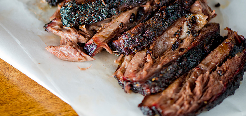 Grilled slices of pork barbecue are sitting on a white plate.