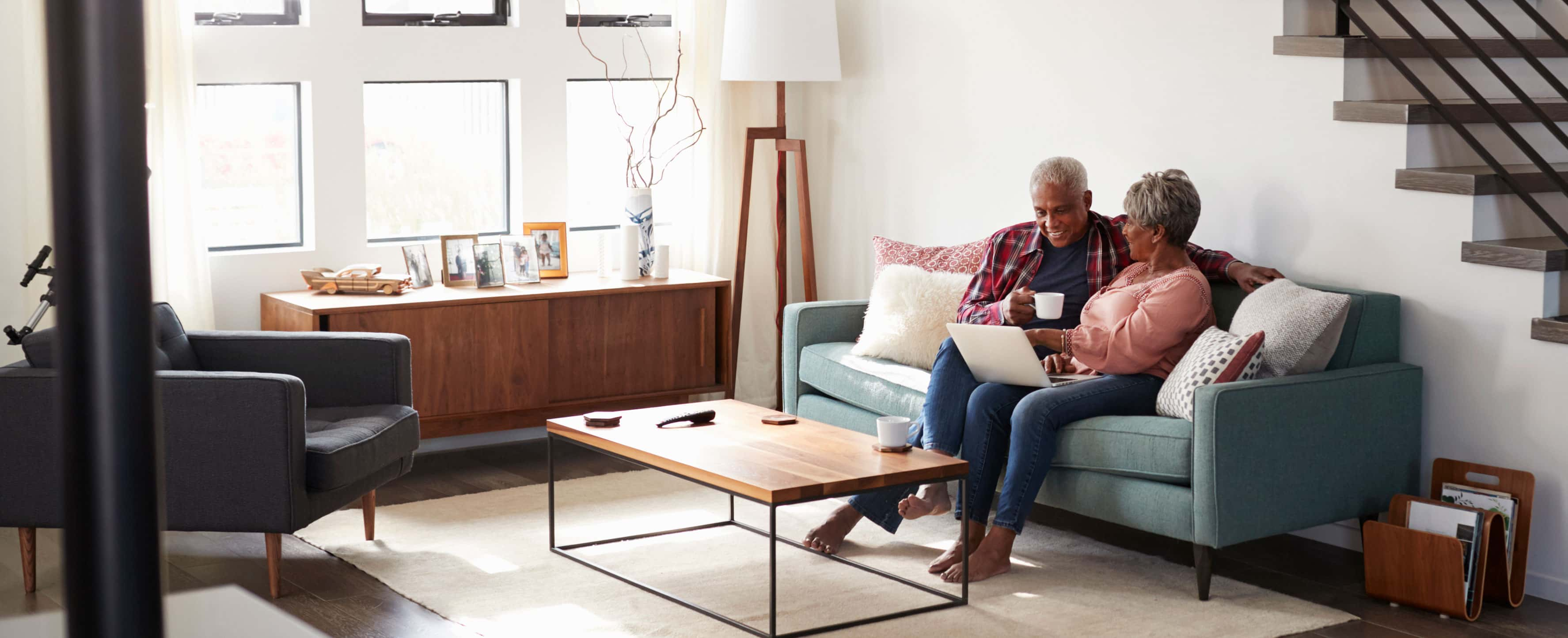 An older couple sit on a living room couch looking together at a laptop.