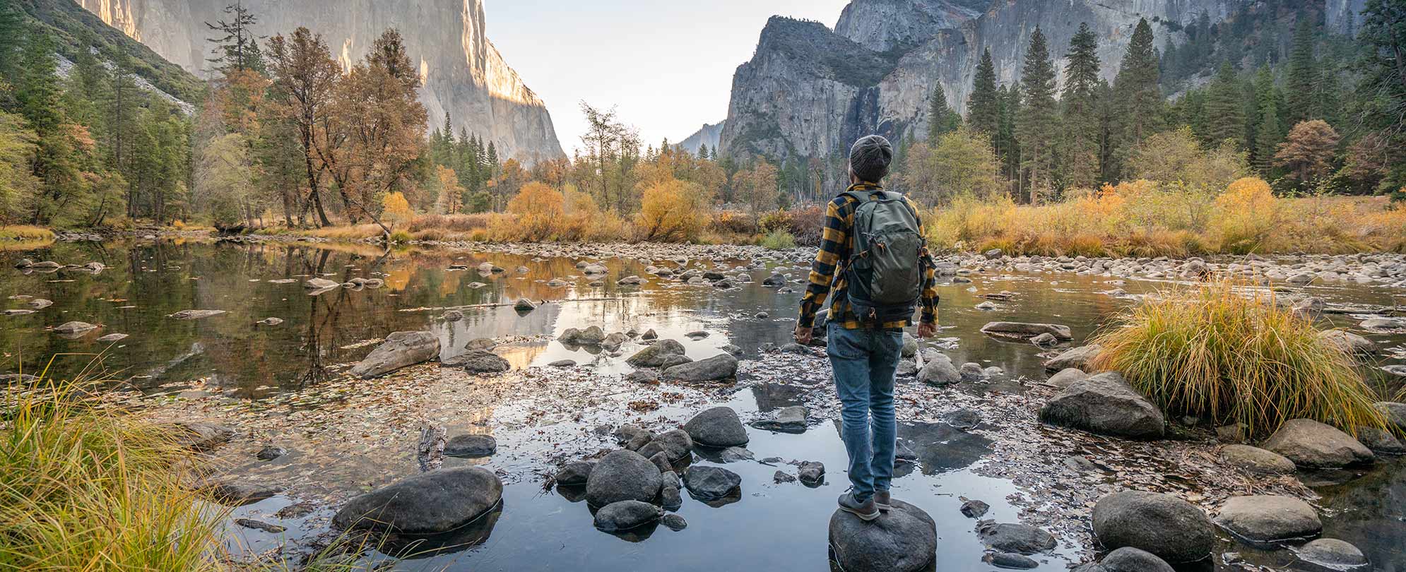 A hiker standing on a rock in shallow water overlooking a mountainous landscape