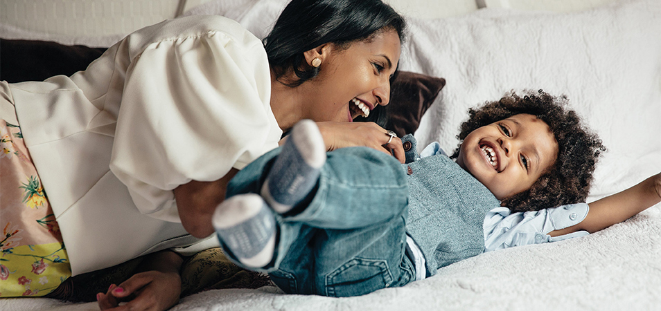 A mother is tickling her baby boy on his belly.