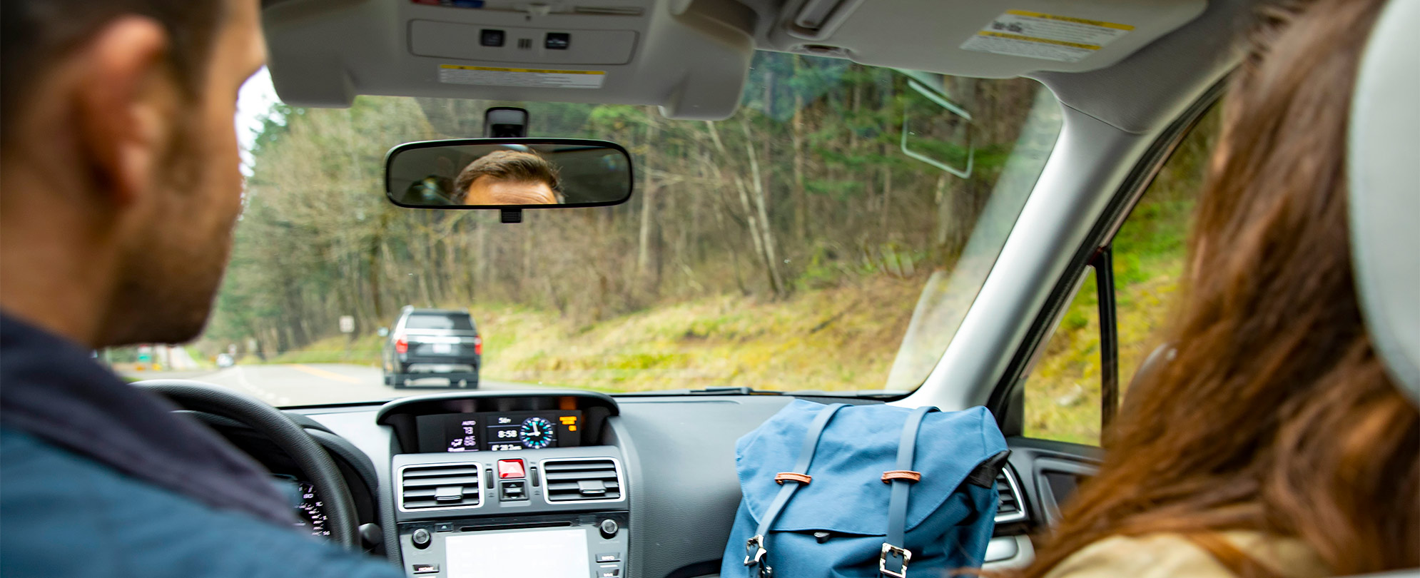 A man and woman in the front seats of a car, the woman is holding a WorldMark by Wyndham backpack on her lap.