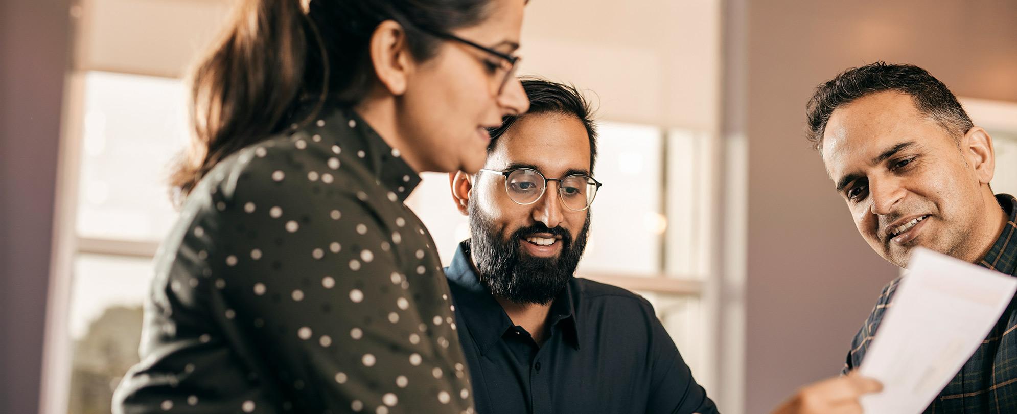 One woman and two men look down at a piece of paper. 