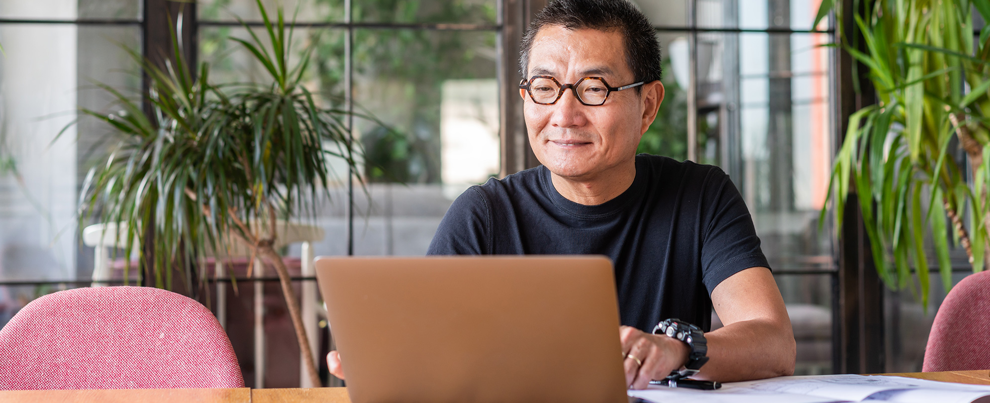 An older man sitting at a table and looking at his laptop. 