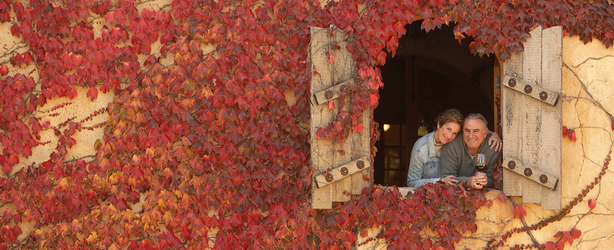 A couple, standing in the window of a European villa covered in red vines.