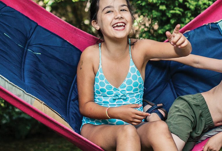 A young girl and boy wearing swimsuits sit in a hammock.