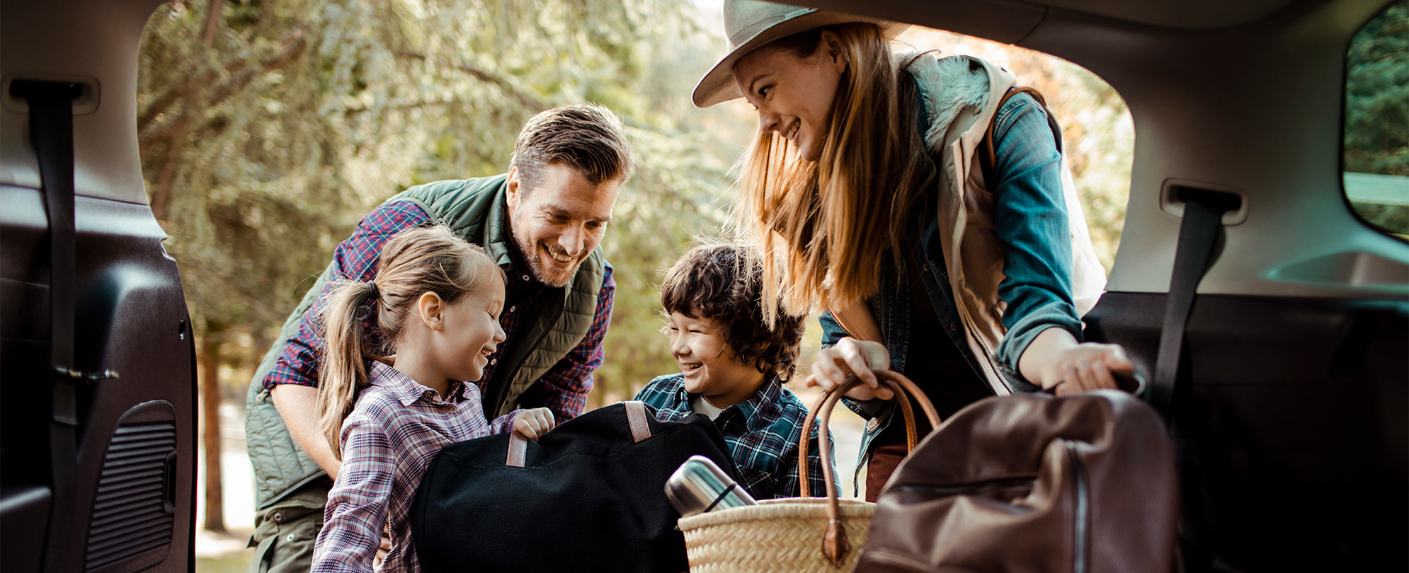 Mom, dad, and two young kids put suitcases and backpacks in the backseat of a car for their WorldMark by Wyndham vacation.