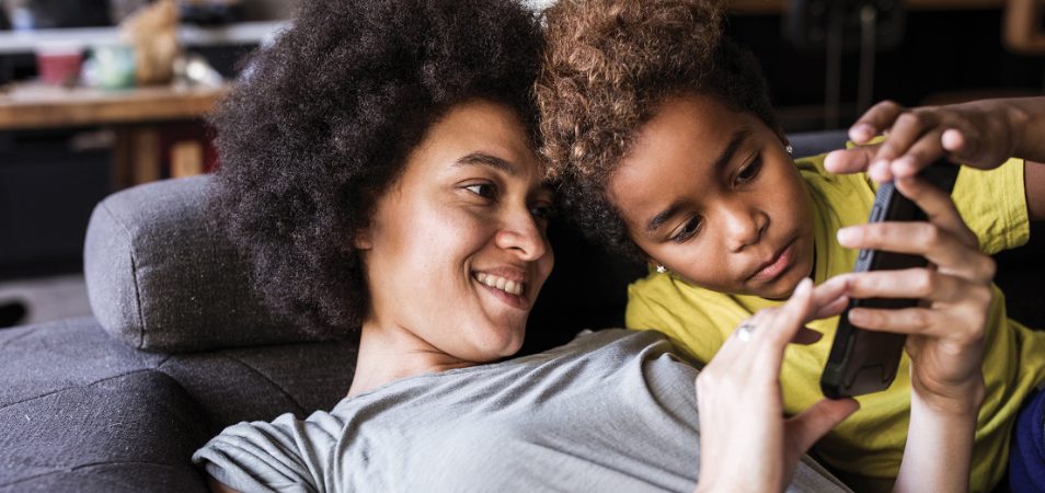 Woman and her son look at a cellphone while laying on the couch of their WorldMark by Wyndham resort suite.