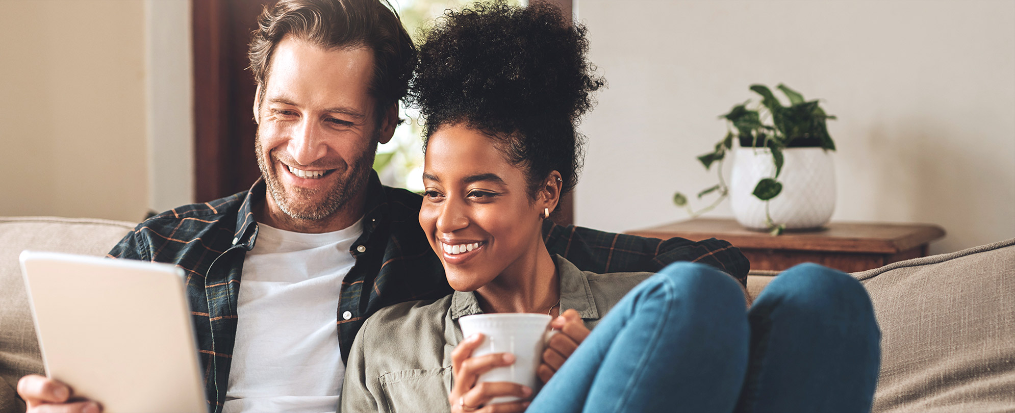 A couple sitting on a couch, smiling while reviewing the Owner Guide on their iPad. 