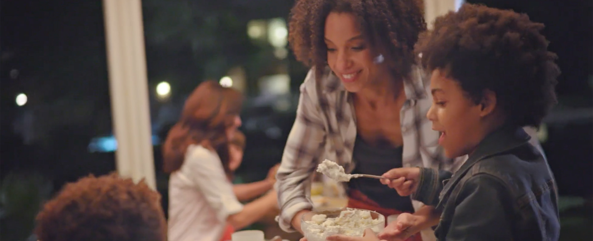 A smiling mom and son serve food with a spoon. 