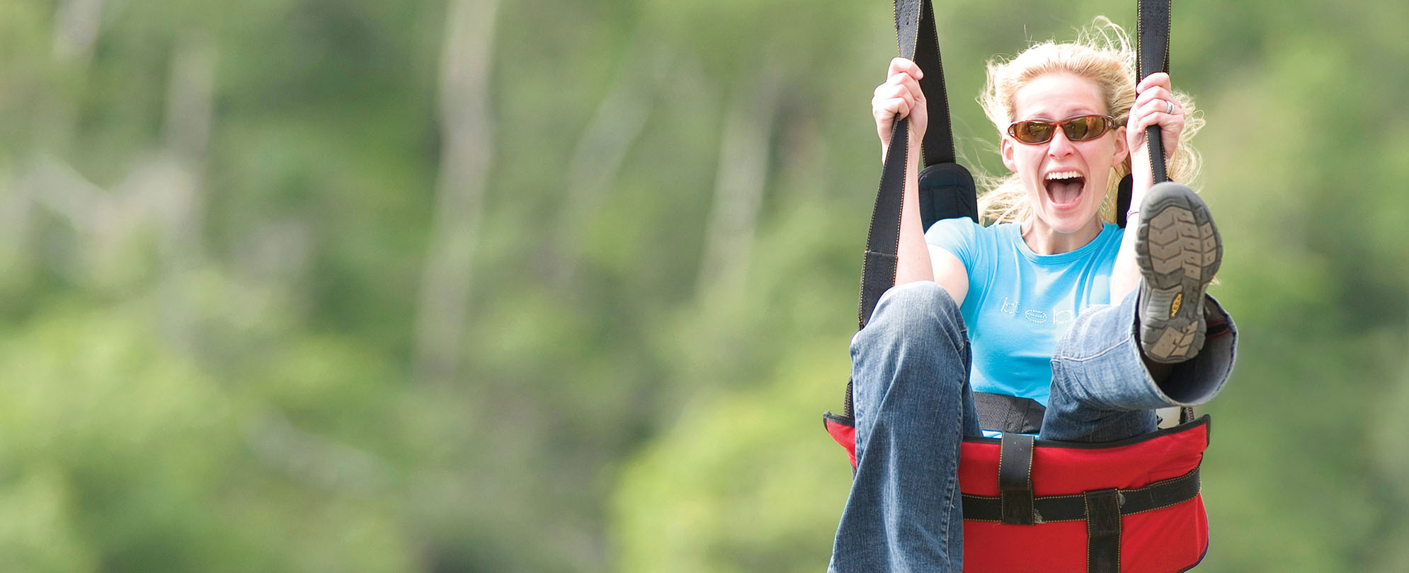 A woman wearing sunglasses smiles excitedly on the Vigilante Extreme Zip-Rider in Branson, Colorado.