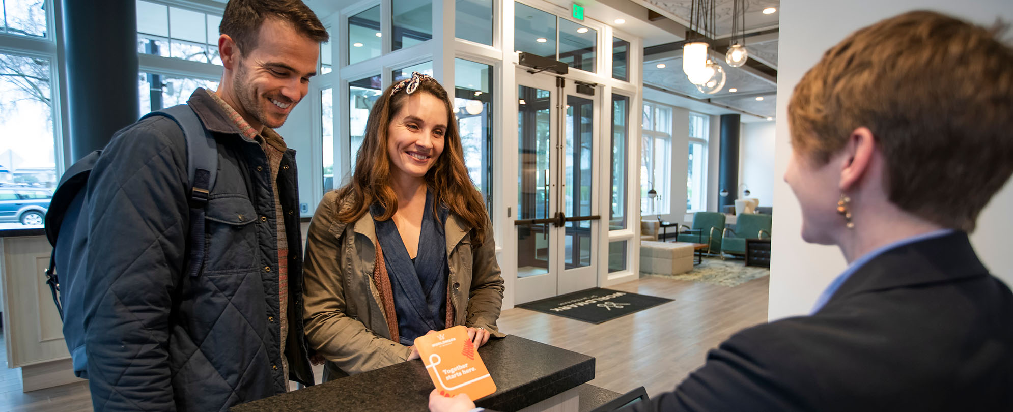 A man and woman smile at a WorldMark employee standing at the resort front desk.