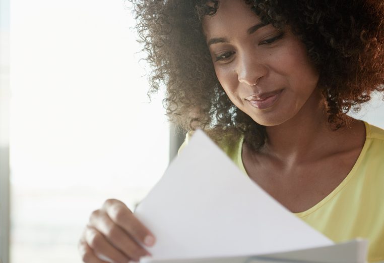 A woman with curly hair smiles looking down at the papers she is holding.