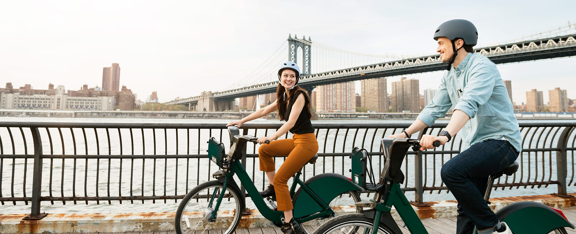 Happy couple bikes past a bridge in New York City, one of many Club Wyndham destinations available to WorldMark owners through Wyndham Club Pass.