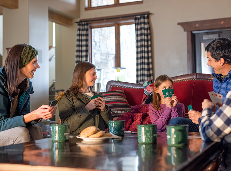 Mom, dad, son, and daughter play cards in the living room of their WorldMark by Wyndham resort suite.